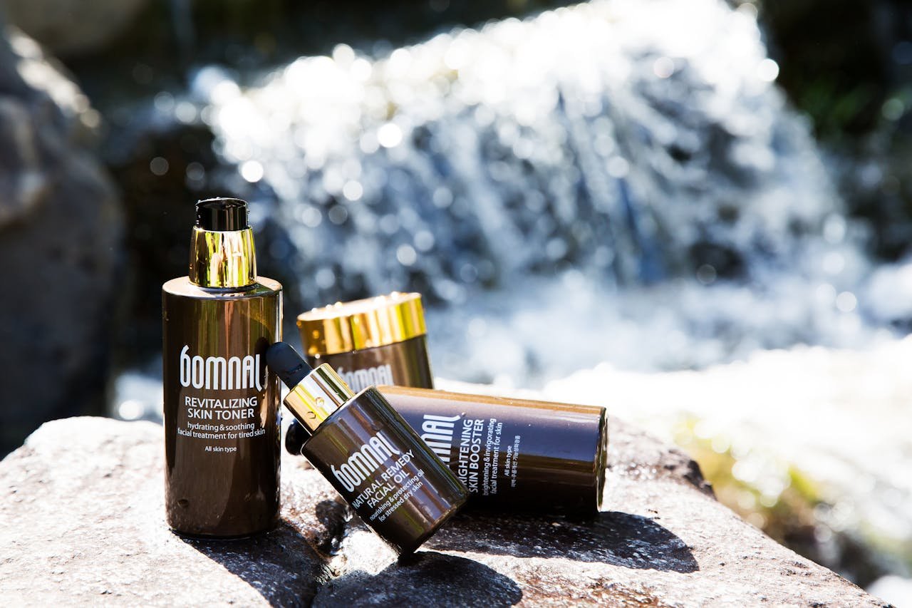 Close-up of Bomnal skincare products displayed on rocks by a waterfall, showcasing their luxurious packaging.